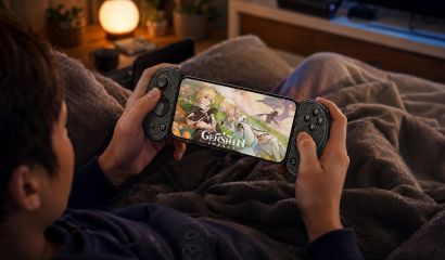 Gamer playing Genshin Impact on a smartphone with a mobile gaming controller while relaxing in bed, showcasing a handheld gaming setup for cloud and mobile gaming.