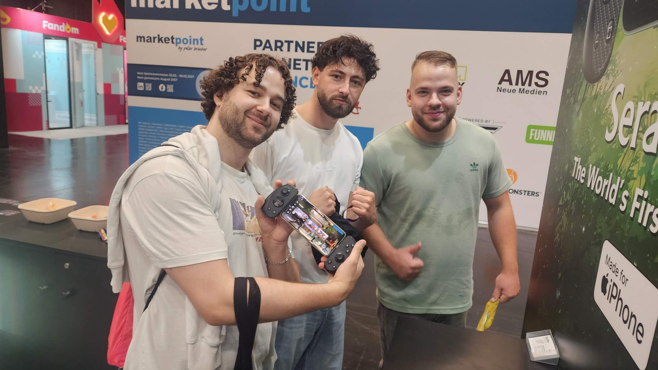 Three Gamescom 2026 attendees posing with the Serafim S3 mobile gaming controller at the Serafim booth in Cologne.